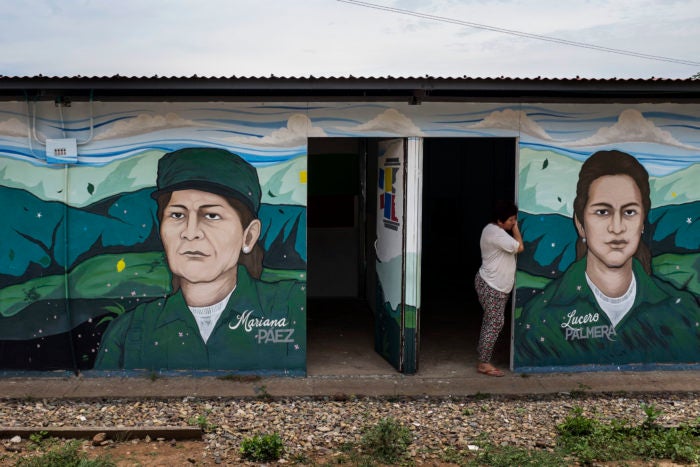 Picture of woman standing at the doorway of a building. The building has murals of Mariana Paez and Lucero Palmera on it