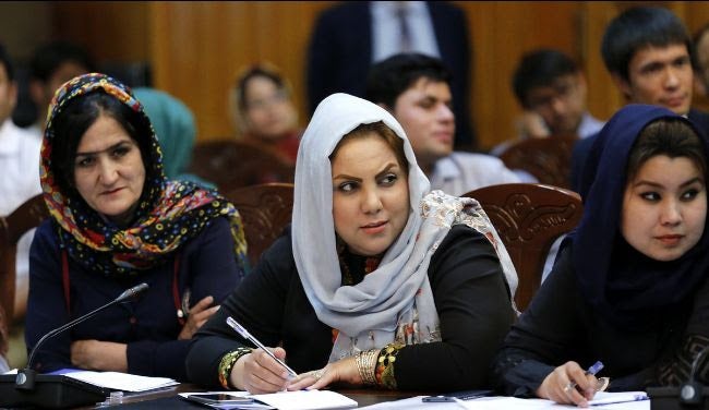 Afghan women taking notes at an event. There is a microphone at their table