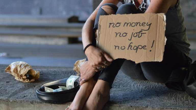 Image of a homeless woman with a sign that says "No money, no job, no hope."