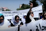 A group of Afghan women march in the street holding a large sign.