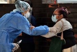 Photo of two women wearing medical masks and personal protective equipment holding one another by the forearm.