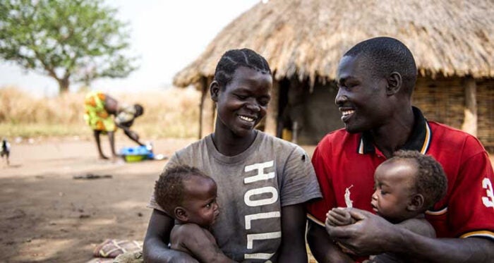 A man and woman smile at one another while each holding a small child.