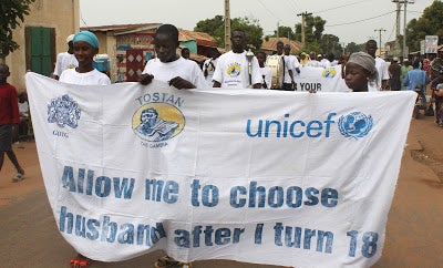 A group of young women march down a street holding a banner that reads "all me to choose my husband after I turn 18"