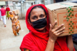 Photo of a woman wearing a face mask and carrying a box over her shoulder.
