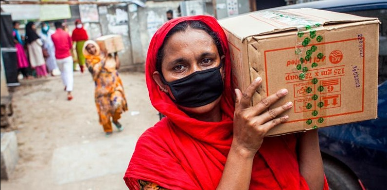 Photo of a woman wearing a face mask and carrying a box over her shoulder.