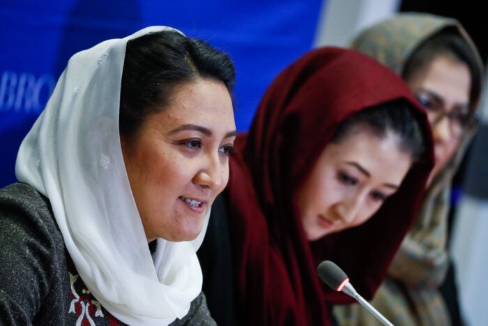 An image of Afghan women politicians speaking at a formal panel discussion is included for decorative purposes.